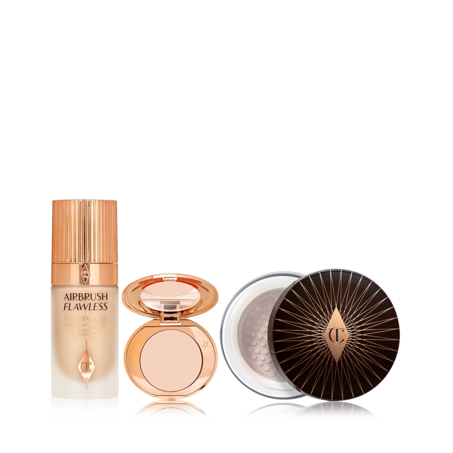 Foundation in a glass bottle with a gold-coloured lid, colour corrector compact in a light shade with a mirrored-lid, and loose setting powder with a black and gold-coloured lid. 