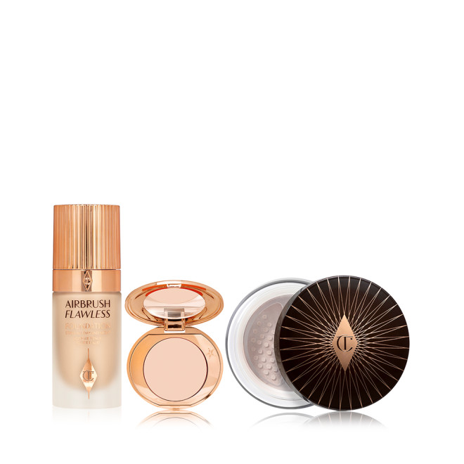 Foundation in a glass bottle with a gold-coloured lid, colour corrector compact in a light shade with a mirrored-lid, and loose setting powder with a black and gold-coloured lid. 
