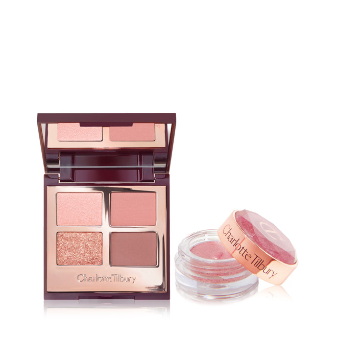 An open, mirrored-lid quad eyeshadow palette in pink and gold shades with a shimmery, cream eyeshadow in a nude-pink shade in a glass pot with its lid removed.