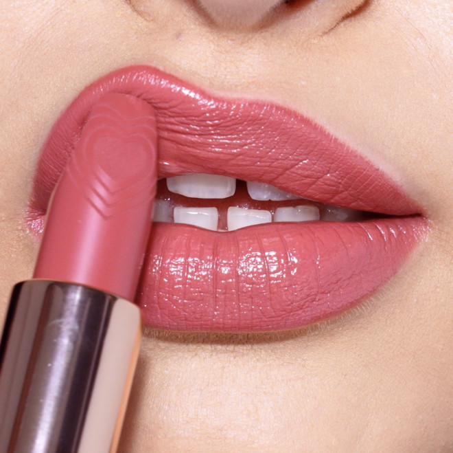 Lips close-up of a fair-tone model applying a rosy pink lipstick with a satin finish.