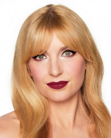 A fair-tone model with green eyes wearing reddish-plum eye makeup, glowy face base, and a vampy-red lipstick with a satin-finish. 