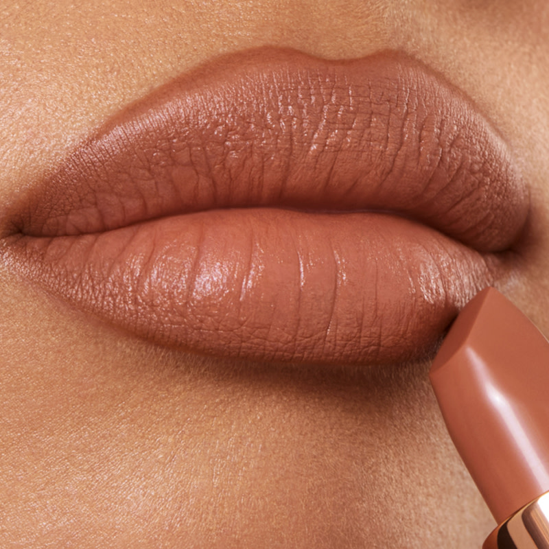 Lips close-up of a medium-tone model applying a brownish-peach-coloured nude lipstick with a matte finish.