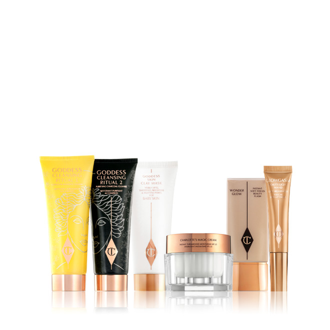 Two facial cleansers, one in yellow packaging and the other in black, with a clay mask in white packaging, a thick pearly white cream in a glass jar, a light beige coloured primer in a rectangular bottle, and a highlighter wand in champagne-gold packaging. 