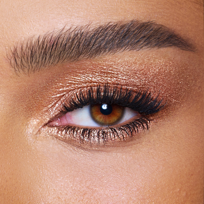 Close-up of a model with brown eyes wearing iridescent orange-gold eyeshadow with very fine shimmer. 