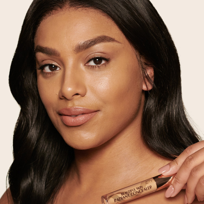 Deep-tone model with brown eyes wearing a radiant, concealer that brightens, covers blemishes, and makes her skin look fresh along with nude lip gloss and subtle eye makeup.