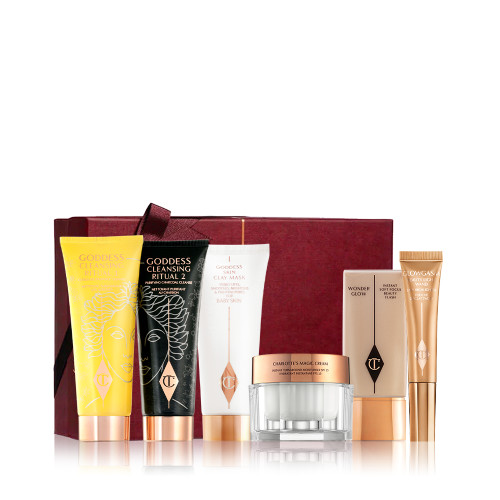 Two facial cleansers, one in yellow packaging and the other in black, with a clay mask in white packaging, a thick pearly white cream in a glass jar, a light beige coloured primer in a rectangular bottle, and a highlighter wand in champagne-gold packaging, with all the products in front of their maroon coloured gift box. 