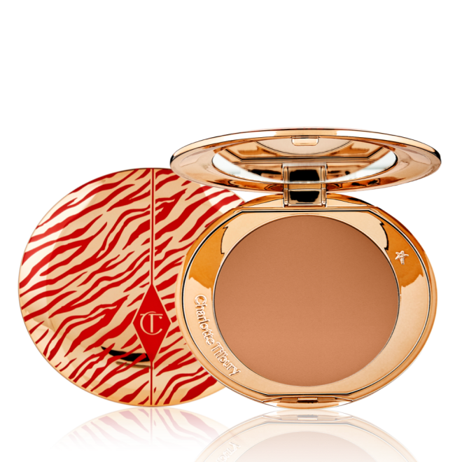 An open, pressed powder compact for deep skin tones with a mirrored lid, in gold-coloured packaging with red-coloured tiger stripes on the lid.