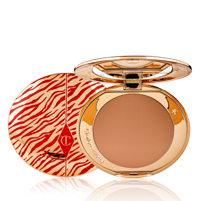 An open, pressed powder compact for deep skin tones with a mirrored lid, in gold-coloured packaging with red-coloured tiger stripes on the lid.