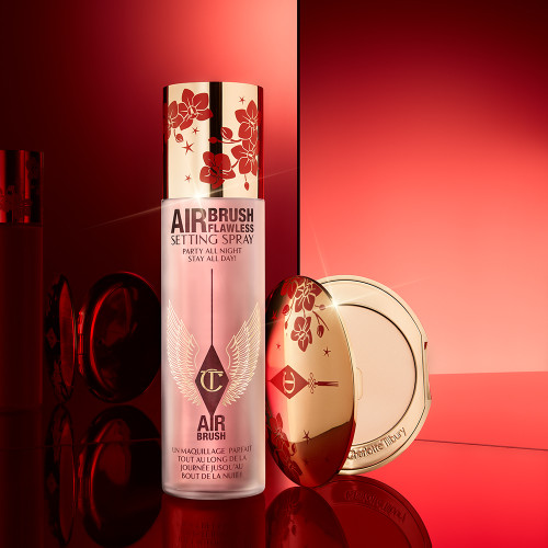 A makeup setting face mist in a large, clear bottle and a setting powder compact, both with gold and red blossom details in celebration of the Lunar New Year