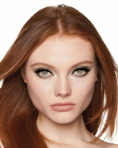 A fair-tone, auburn hair model with grey eyes wearing shimmery green, gold, and khaki eyeshadow with teal and khaki-green eyeliner on the upper lid and lower waterline. 