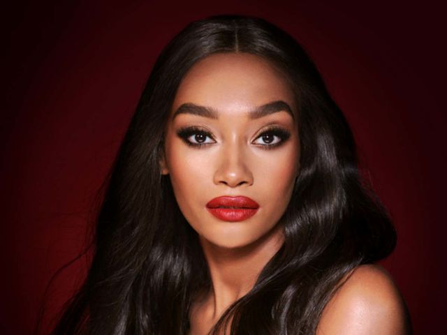 A deep-tone model with brown eyes wearing shimmery bronze eye makeup with muted pink blush and glossy scarlet-red lips