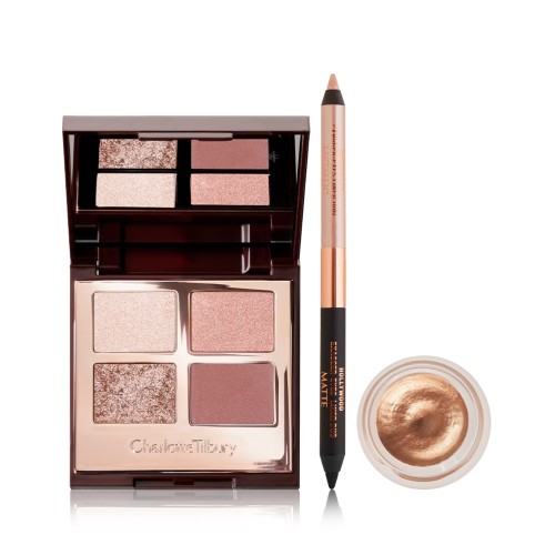 An open, mirrored-lid eyeshadow palette in nude pink and gold shades, double-sided eyeliner pencil in a nude beige and black shades, and cream eyeshadow in a gold shade in an open pot.