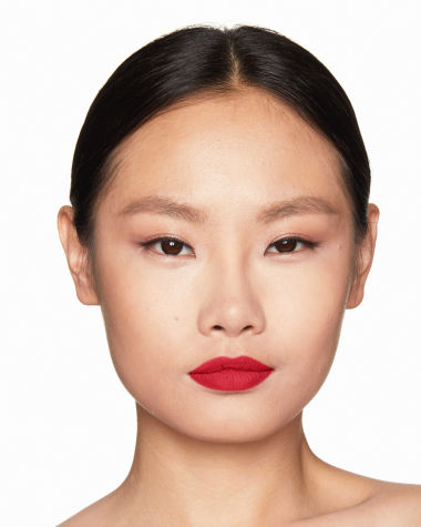 A fair-tone model with brown eyes wearing a matte, bright, cherry-red lipstick.