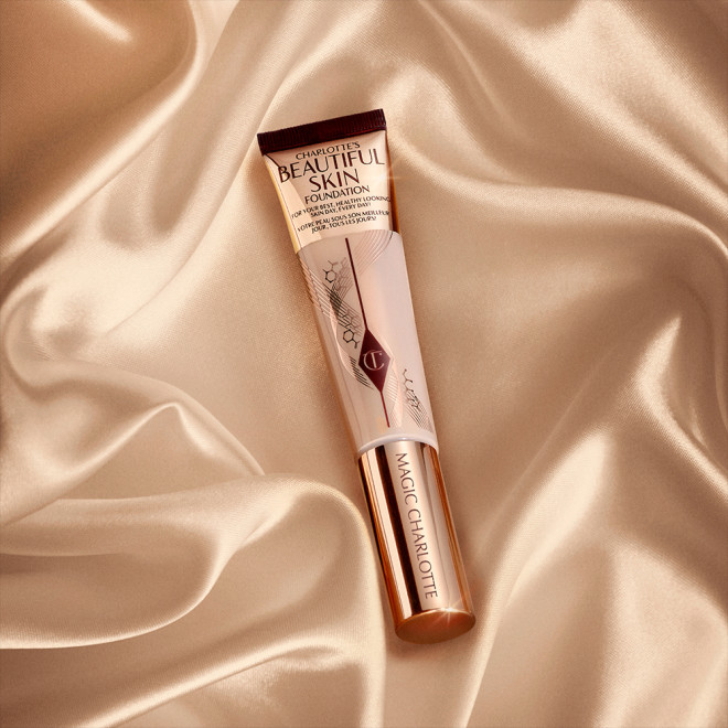 A foundation wand in gold packaging with a pinkish-beige-coloured body to show the shade of the foundation inside, and a gold-coloured lid.