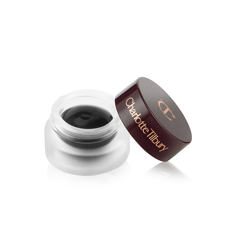 An open frosted glass pot with a cream eyeshadow in a jet-black shade with a matte finish with a dark brown lid with Charlotte Tilbury written on the lid in gold. 