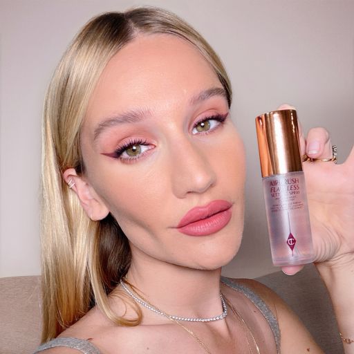 Sofia Tilbury holding a setting spray in a clear bottle with a gold-coloured lid.