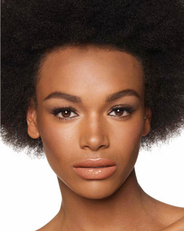 Deep-tone model with brown eyes wearing a plumping champagne-nude lip gloss with gold sparkles.