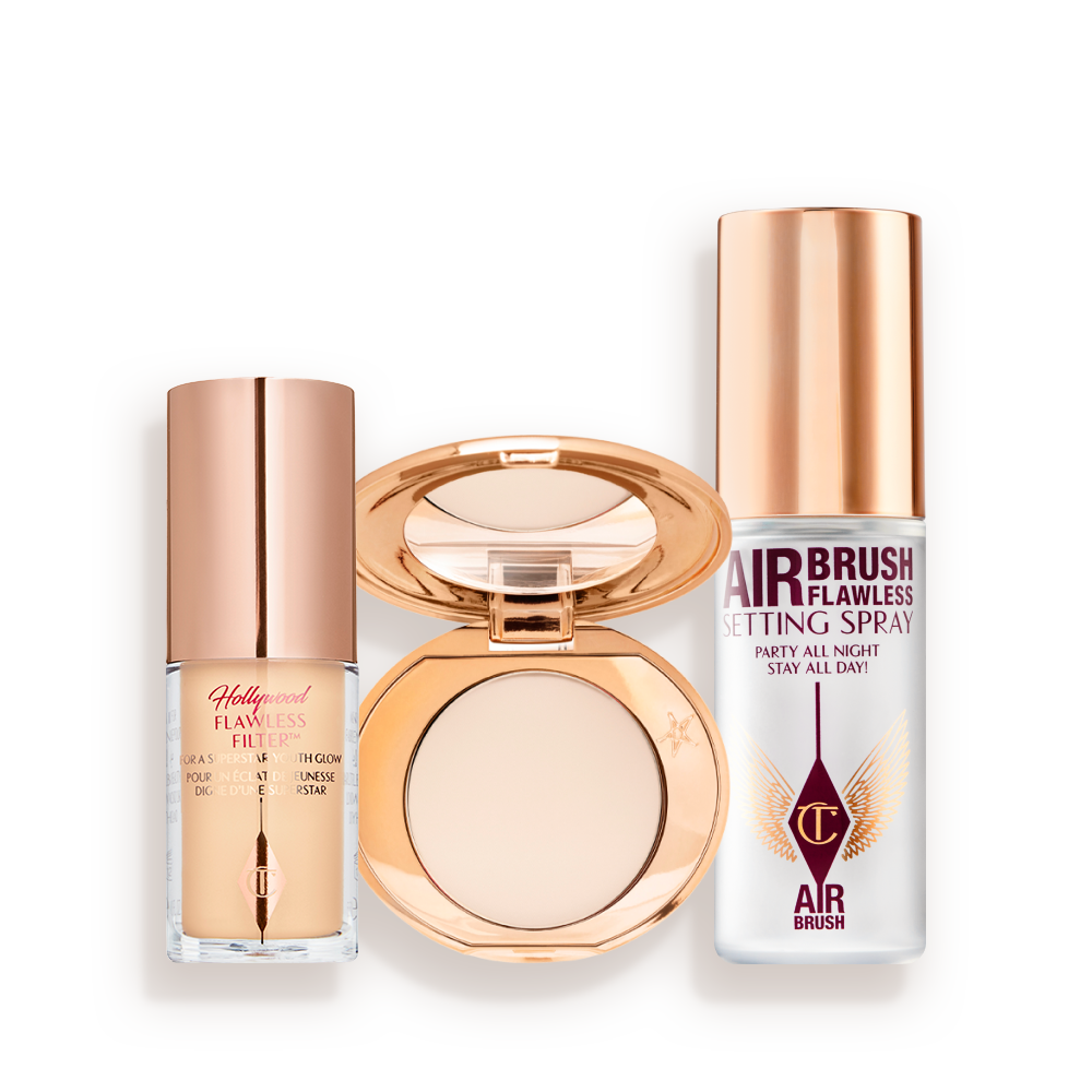 Travel-size kit that includes a glowy primer in a glass bottle with gold-coloured lid, face powder compact in a light shade with a mirrored-lid in gold-coloured packaging, and setting spray in a clear bottle with gold-coloured lid.