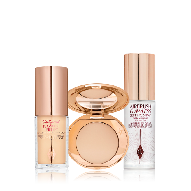 Travel-size kit that includes a glowy primer in a glass bottle with gold-coloured lid, face powder compact in a light shade with a mirrored-lid in gold-coloured packaging, and setting spray in a clear bottle with gold-coloured lid.