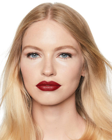 Fair-tone blonde model with blue eyes wearing a muted wine-red lipstick with a satin finish.