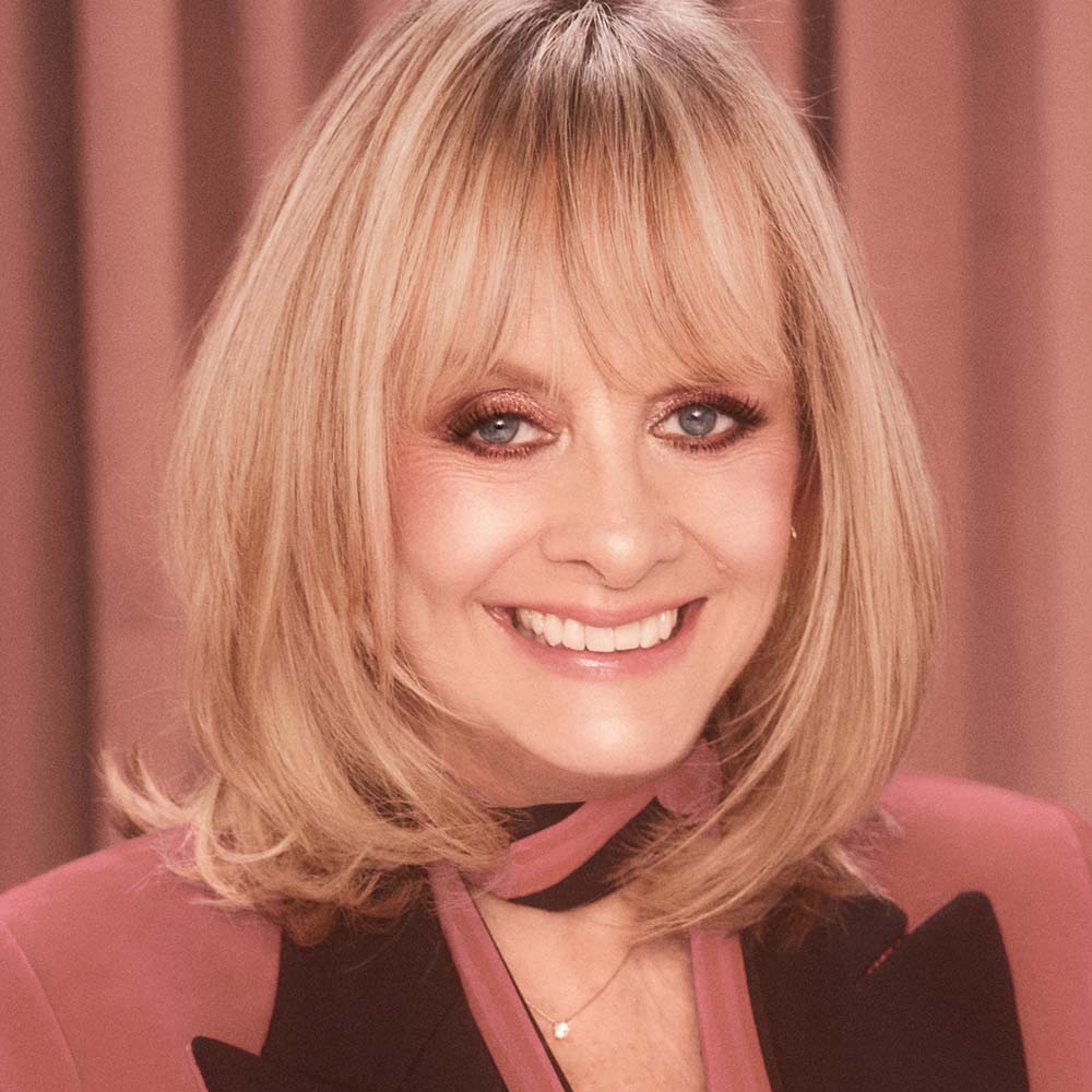 Fair-tone model with mature skin and blue eyes wearing nude pink matte lipstick with shimmery rose gold eye makeup and soft nude pink, glowy blush. 