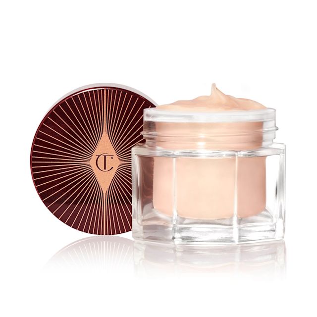 Une crème pour le visage riche et épaisse de couleur champagne foncé dans un pot en verre ouvert avec un couvercle noir et doré à côté.