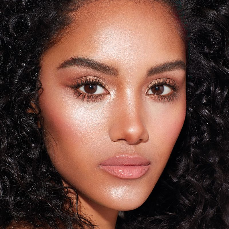 Model wearing glowy, sheer, nude pink makeup with a volumising mascara, and a black eyeliner in a wing shape. 