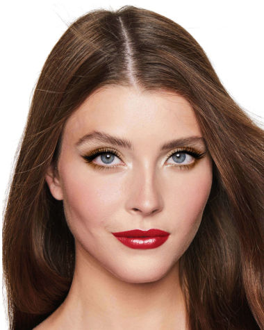 A fair-tone model with blue eyes wearing shimmery bronze eye makeup with muted pink blush and glossy scarlet-red lips