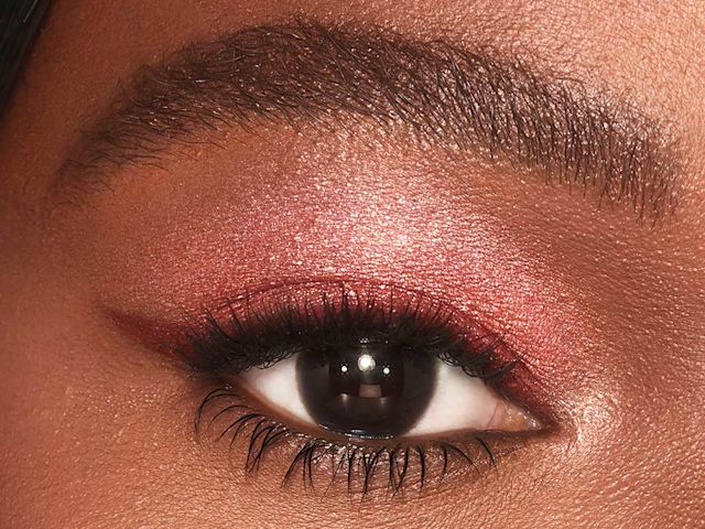 Single-eye close-up of a deep-tone model with brown eyes wearing shimmery berry-pink eyeshadow.