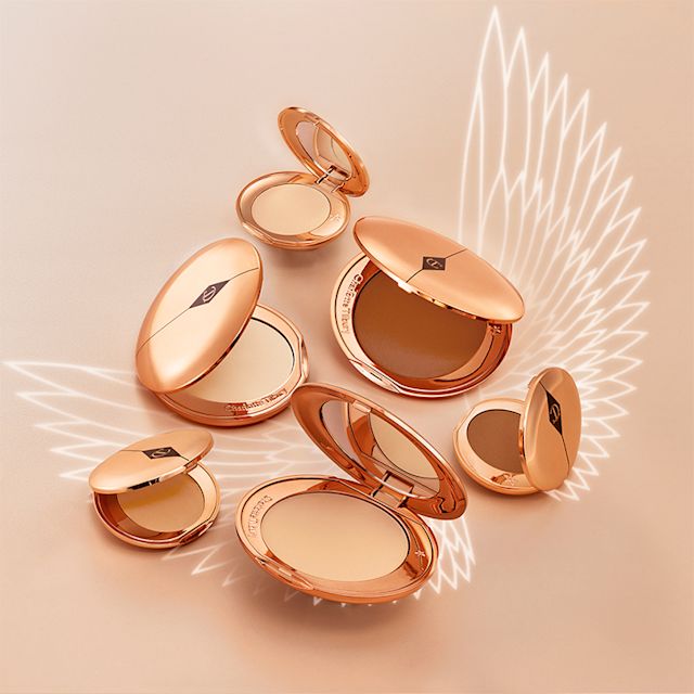 A collection of pressed powder compacts for light, medium-light, fair, and deep tones, in gold-coloured packaging with mirrored lids.