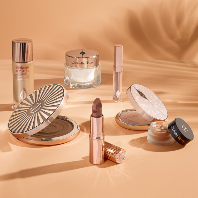 An open nude terracotta lipstick in golden-coloured packaging, open cream bronzer compact in a dark brown shade, SPF-infused primer in white packaging, and cream eyeshadow in a dark gold shade with a dark brown lid.
