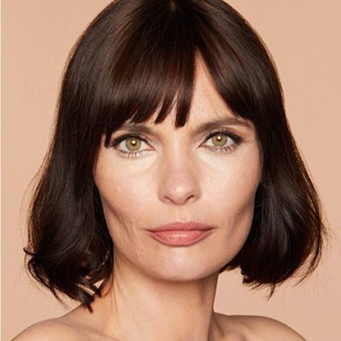 Une mannequin aux cheveux brun et à la peau mature claire éclatante, portant un rouge à lèvres mat de couleur pêche nude et un ligneur noir.