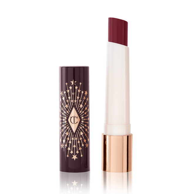 An open lipstick lip balm in a berry shade, in white and gold tube with a black-coloured lid with gold sparkles all over it.