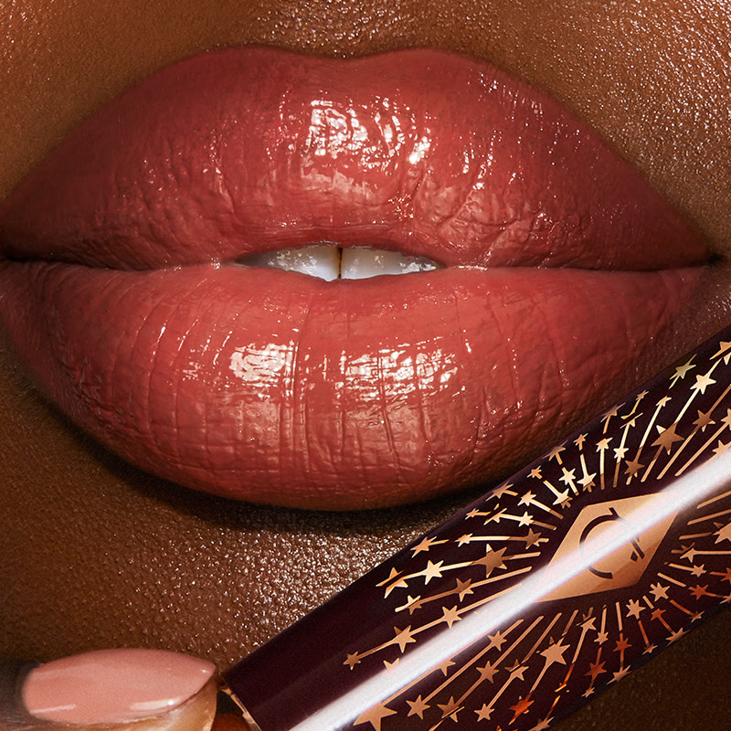 Lips close-up of a deep-tone model wearing a glossy soft coral lipstick lip balm. 