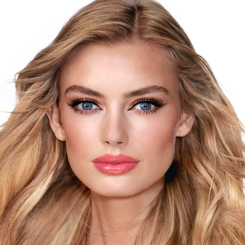 A fair-tone model with blue eyes wearing soft fawn and brown eye makeup with glowy terracotta blush, and sheer, glossy rose-pink lips.
