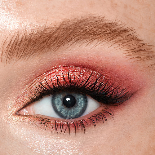 Single-eye close-up of a blue-eyed fair-tone model wearing shimmery rose gold, fawn, and berry-pink eye makeup.