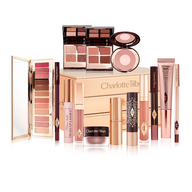 Pillow Talk Dreams Makeup Vault Box with products A reflective, gold-coloured chest with two drawers containing makeup items, which include Liquid highlighter wand in rose gold, black mascara, shimmery lip gloss in nude pink, glitter-free but high-shine lip gloss in nude pink, rose gold eyeshadow pigment in a petite pot, two closed lipsticks, travel-size lip gloss in nude pink, eyeliner pencil in dark brown, lip liner pencil in nude pink, quad eyeshadow palettes, 12-pan eyeshadow palette, and two-tone blush compacts.