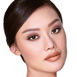 A fair-tone model with brown eyes wearing smokey brown eye makeup with muted pink blush with glossy soft-brown lips.