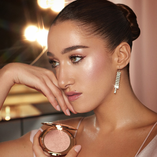 Bella Tilbruy wearing dew makeup with smokey eye makeup, nude lipstick, and glowy powder highlighter in a rose gold shade.