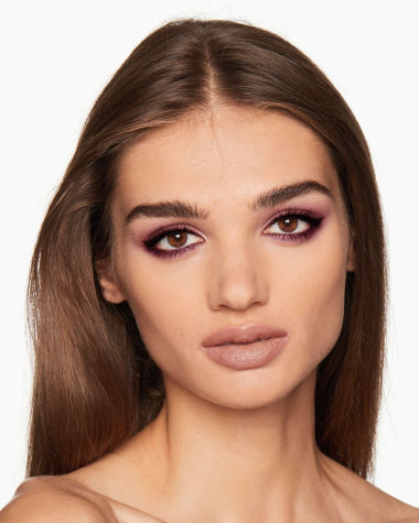 A medium-tone brunette model with brown eyes wearing shimmery maroon, copper, and gold eye makeup along with plum eyeliner. 