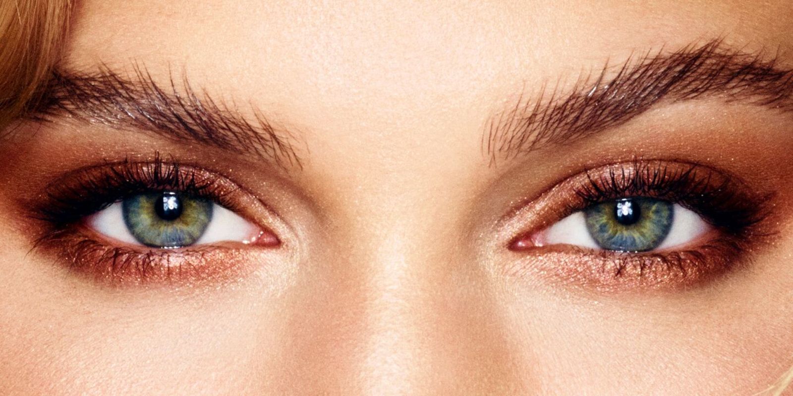 Nahaufnahme von dunklen Augenbrauen und grün blauen Augen, die mit bronze Lidschatten geschminkt sind. 