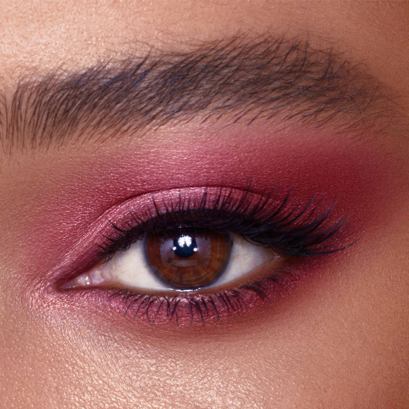 Eye close-up of a deep-tone model with brown eyes wearing plum-coloured eye makeup. 