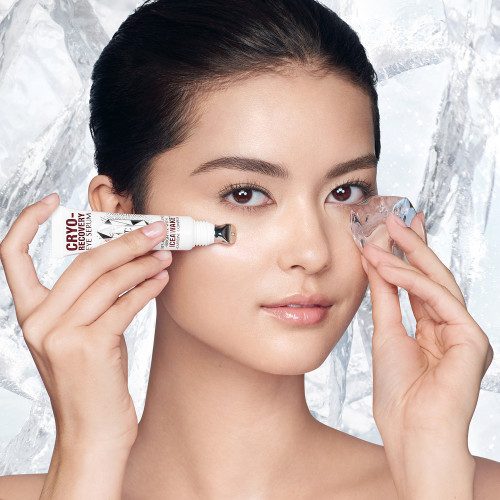 Fair-tone model with flawless, poreless, and glowy skin applying a white-coloured eye serum under her one eye and massaging an ice cube on the other side for a depuffing, cooling, and relaxing her skin. 