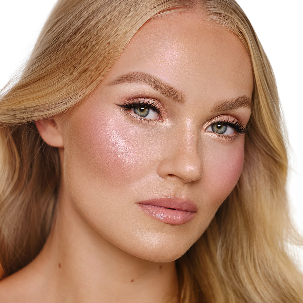 Blonde fair skin model wearing a soft glam makeup look with winged eyeliner, rosy glowing cheeks and nude lip