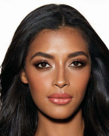 A deep-tone model with brown eyes wearing smokey brown eye makeup with warm bronze and pink blush, and glossy terracotta lips.