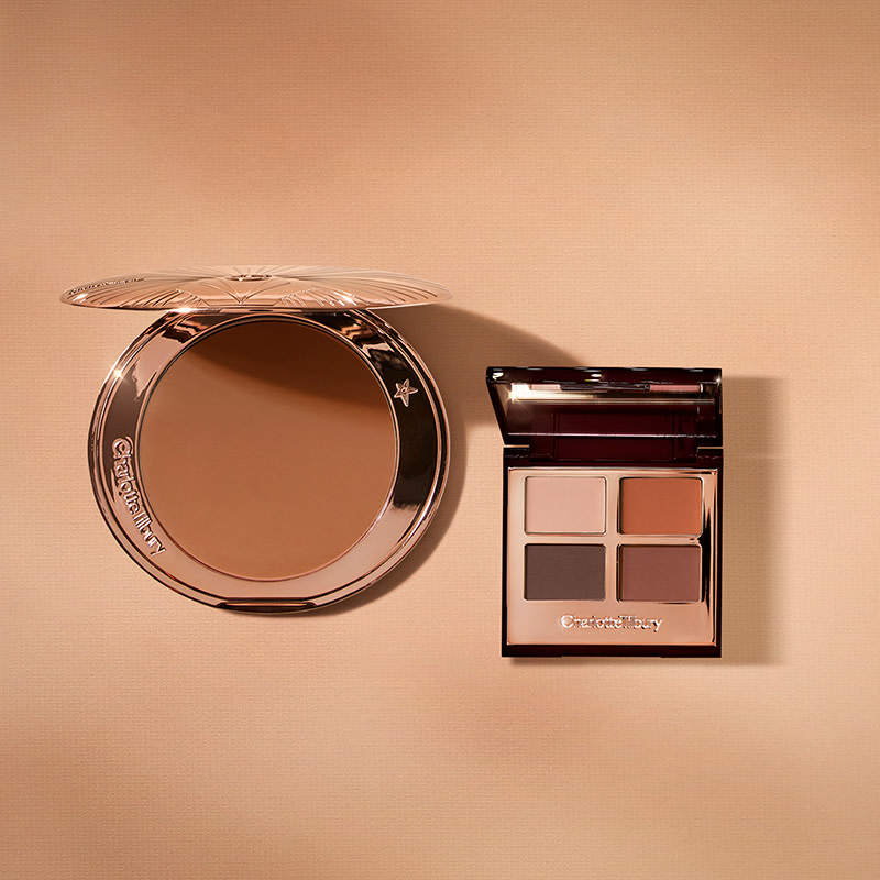 An open bronzer in medium-brown shade in golden-coloured compacts with an open, mirrored lid eye shadow palette with four matte and shimmery eye shadows in shades of brown and champagne.