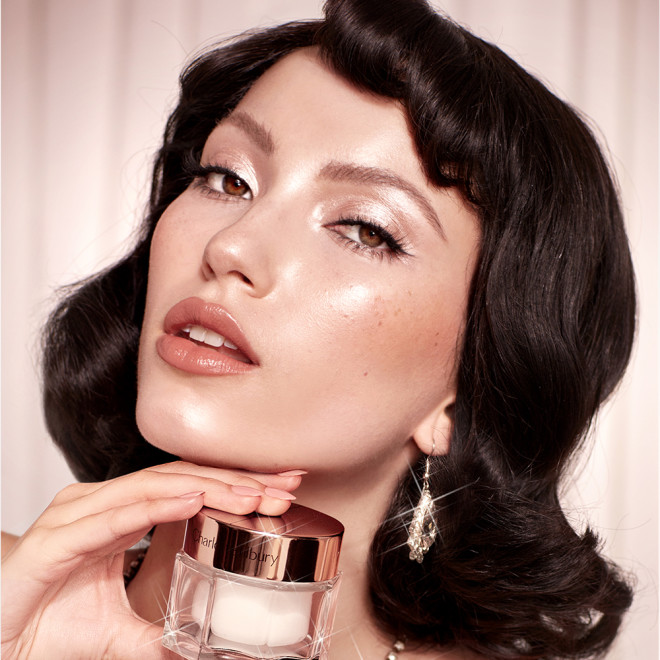 Banner with a fair-tone brunette model with glowy, glass skin, holding a jar of pearly-white face cream with a golden-coloured lid