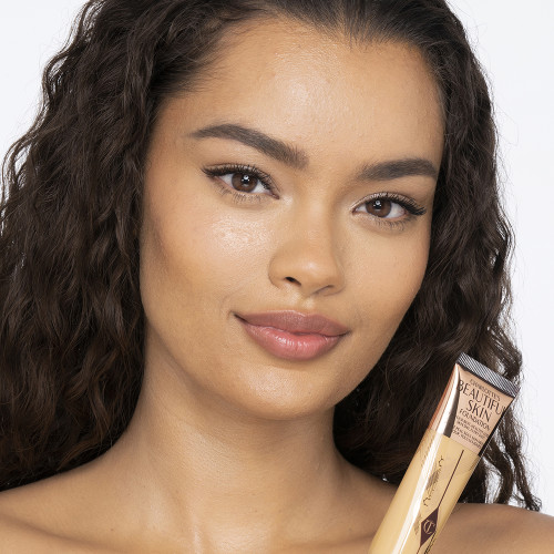 A medium-dark-tone brunette model wearing glowy, skin-like foundation that covers her blemishes and gives the appearance of clean, bouncy, and fresh skin. 