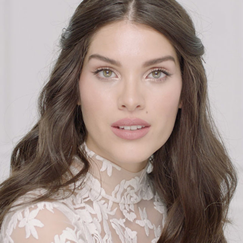 A fair-tone brunette bride with a flawless, glowy base wearing glossy bright pink lipstick with muted, nude pink makeup. 