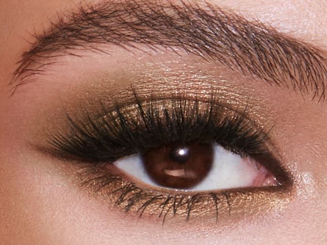 Single eye close-up of a brown eye with shimmery gold and khaki eyeshadow with thick false lashes.